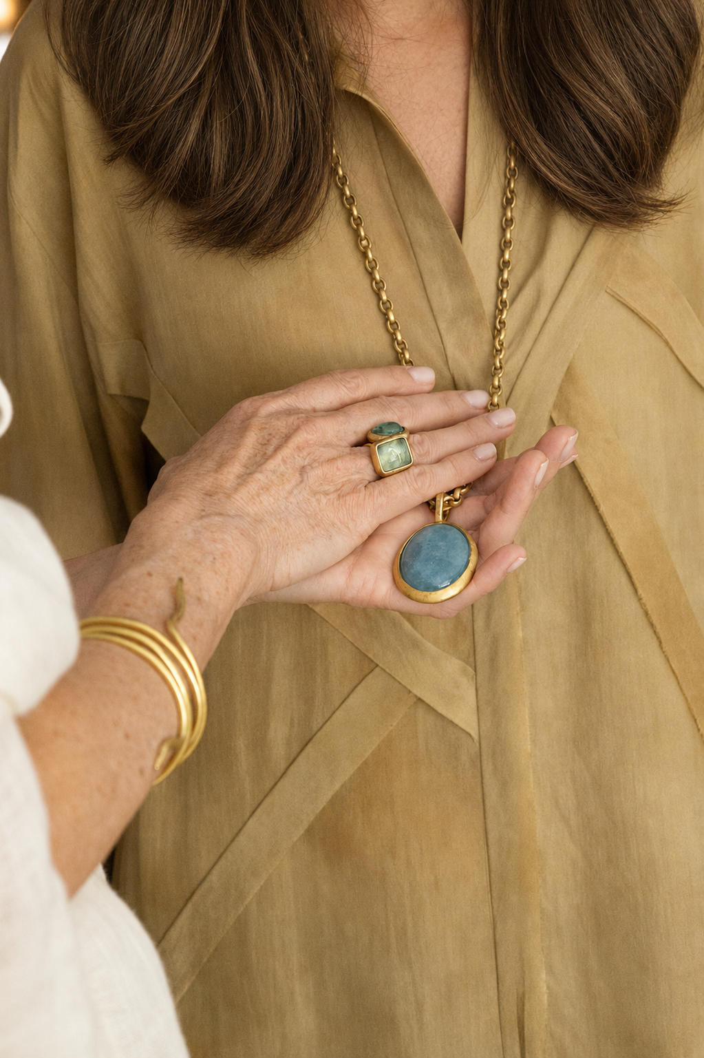 manos de mujer sujetando collar de cadena con Medallón Aguamarina, Brazalete Senda y anillo 